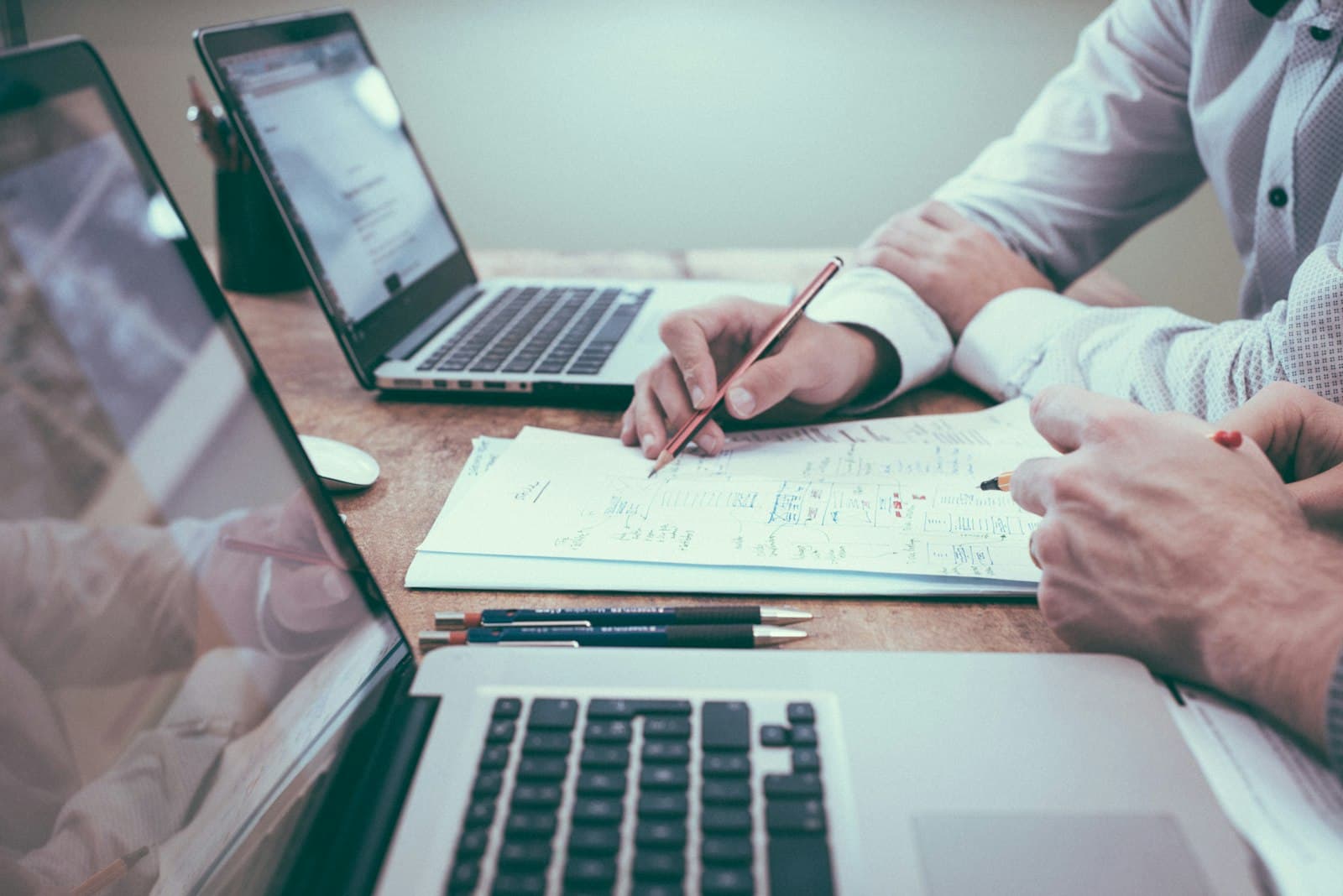 Two people working through plans on paper beside their laptops